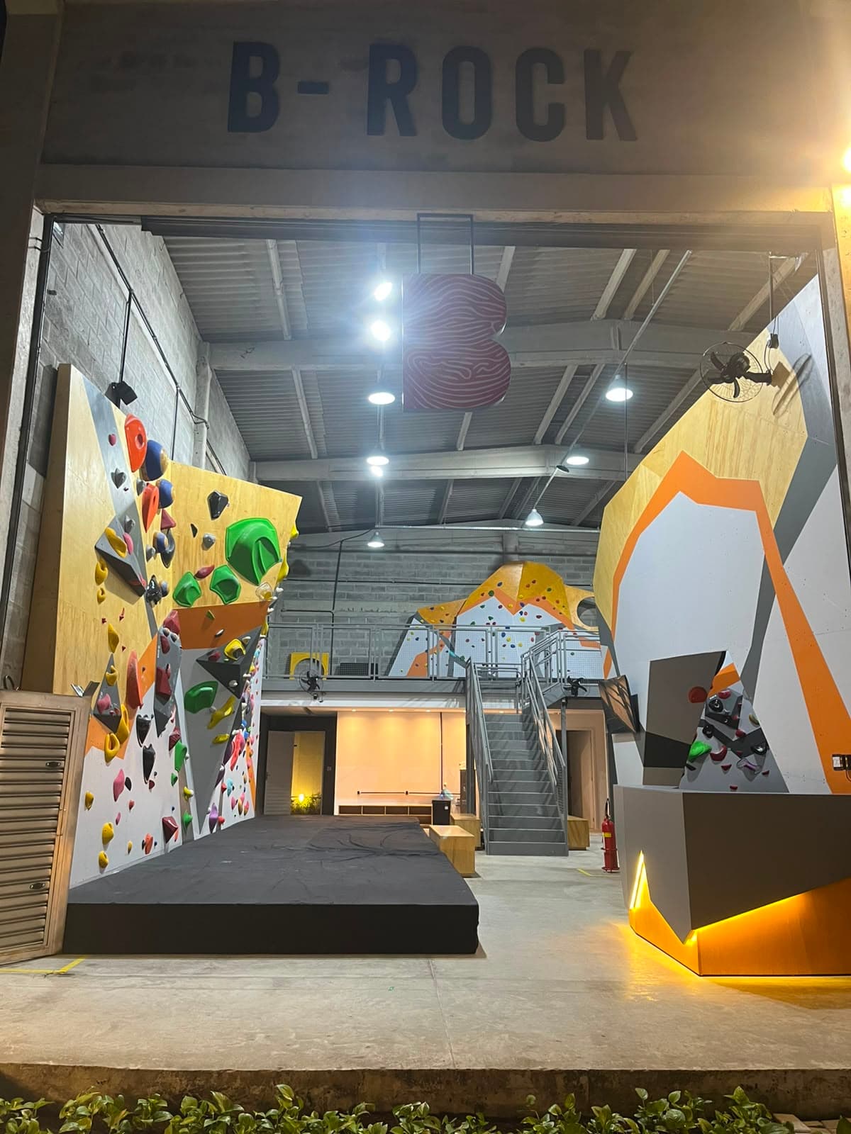 Fachada da B-ROCK à noite, com o letreiro da academia e as paredes de boulder visíveis desde a entrada
